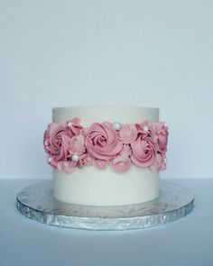 a white and pink cake with flowers on the top is sitting on a silver platter