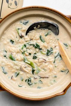 a bowl of soup with noodles and spinach in it next to a wooden spoon