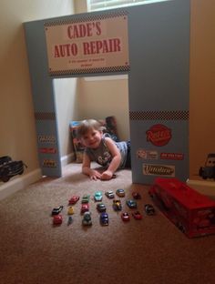 a young boy laying on the floor in front of a car repair sign and toy cars