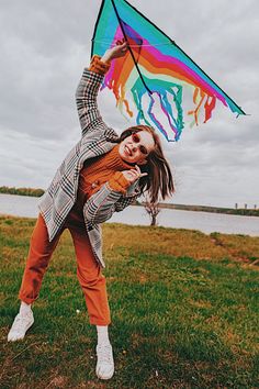 a woman holding onto a colorful kite on top of a green grass covered field with water in the background