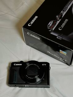 a black camera sitting on top of a white bed next to a box with it's lid open