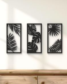 three black metal wall art pieces hanging on a white wall next to a wooden dresser