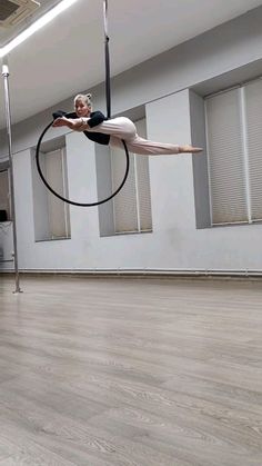 a woman is doing aerial tricks on a hoop in the middle of an empty room