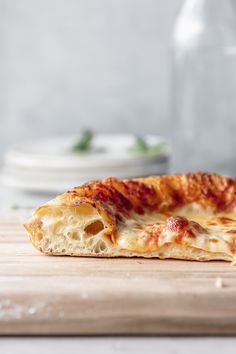 a piece of pizza sitting on top of a wooden cutting board next to a bottle of wine