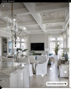 a large open concept living room and dining area with white furniture, chandelier, marble countertops, and exposed wood ceiling