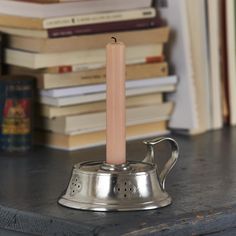 a candle is sitting on top of a pewter with books in the back ground