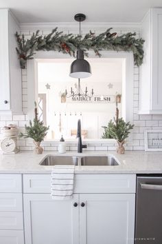 a kitchen decorated for christmas with greenery on the windowsill and wreaths hanging over the sink