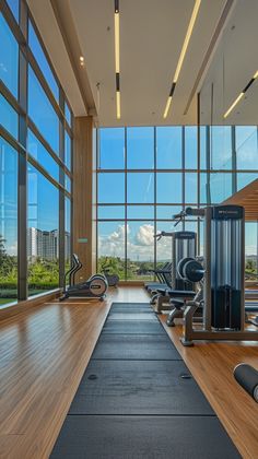 an empty gym with lots of machines and exercise mats in front of large glass windows