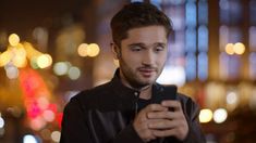 a man looking at his cell phone while standing in front of a cityscape