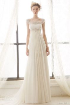 a woman standing in front of a window wearing a white wedding dress with sheer tulle