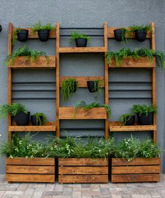 several wooden planters filled with plants on top of a brick floor next to a gray wall