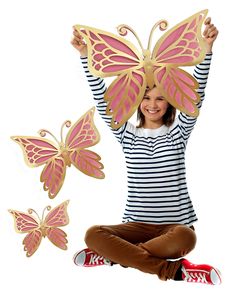 a woman sitting on the ground holding up two pink and gold butterfly shaped cut outs