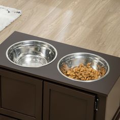 two metal bowls with food in them sitting on top of a wooden cabinet next to a rug