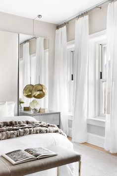 a bedroom with white curtains and a large bed in front of a mirror on the wall