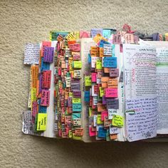 an open book covered in lots of different colored paper notes and writing on top of each other