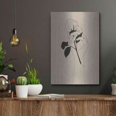 some plants are sitting on a table in front of a gray wall with a black and white painting