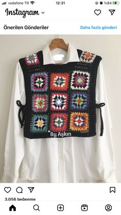 a black and white crocheted sweater hanging on a hanger next to a white shirt