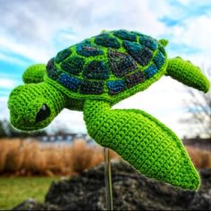 a green crocheted turtle sitting on top of a wooden stick