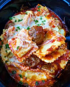 a close up of food in a crock pot with meatballs and cheese on top