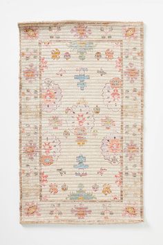 an antique rug is displayed on a white wall with pink and orange flowers in the middle