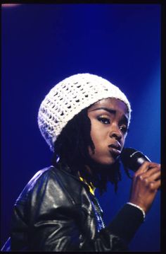 a woman wearing a white crochet hat and holding a microphone in her hand