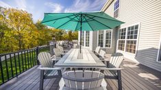 an outdoor table and chairs on a wooden deck with green umbrella over the dining area