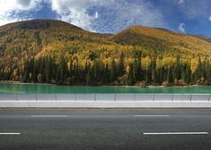 an empty highway with mountains in the background and trees on both sides that are changing colors