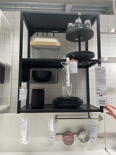 a kitchen with white tile walls and black shelving units on the wall, holding various items for sale