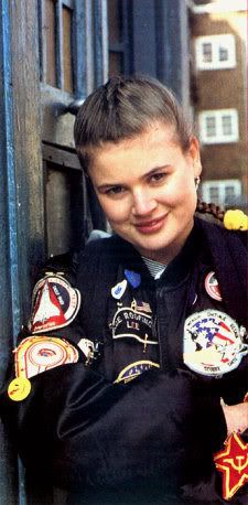 a woman in uniform is smiling and leaning against a wall with badges on her arm