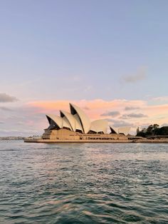 the sydney opera house is seen from across the water at sunset, with pink clouds in the background