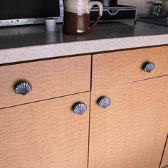 a wooden cabinet with seashells on the front and side drawers next to a microwave