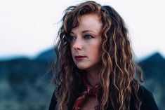 a woman with long curly hair wearing a red neck tie and looking off into the distance