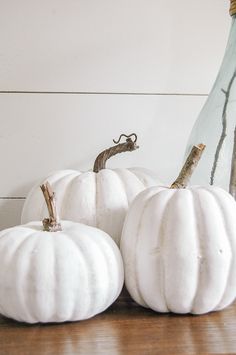 three white pumpkins sitting on top of a wooden table