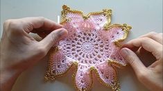 two hands are working on a crocheted doily with gold trimmings