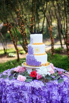 a three tiered cake sitting on top of a table covered in purple and white flowers