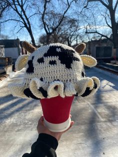 a hand holding up a cup with a knitted cow hat on top of it