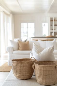 two wicker baskets sitting on top of a table next to a white couch in a living room