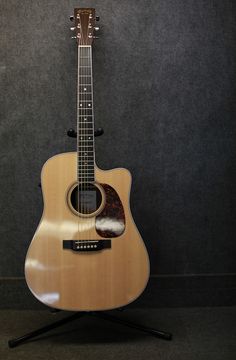 an acoustic guitar sitting on top of a stand in front of a gray wall and black carpet