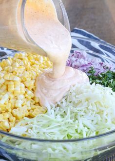 corn, coleslaw, and dressing being poured into a glass bowl on top of a table