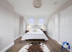 an empty bedroom with white walls and wood flooring is pictured in this image, there are two windows above the bed