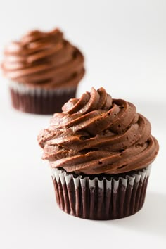 two cupcakes with chocolate frosting sitting on top of each other in front of a white background