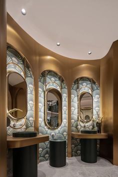 the interior of a modern bathroom with round mirrors and gold accents on the walls, along with black pedestals