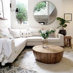 a living room with white furniture and a round mirror on the wall above the coffee table