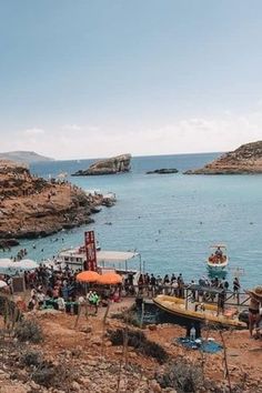 many people are on the beach and in the water near some cliffs, with boats