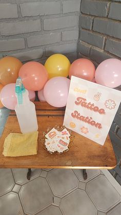 a wooden table topped with lots of balloons and a bottle filled with liquid next to a sign