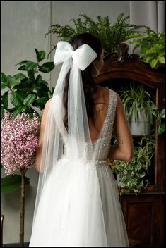 the back of a bride's wedding dress with a white bow on her head