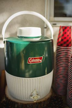 a green and white cooler sitting on top of a wooden table next to red plates