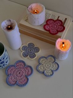 crocheted coasters and candles on a table next to a book, candle