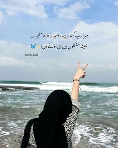 a woman standing on top of a sandy beach next to the ocean with her hand in the air