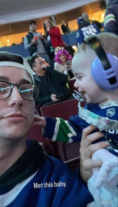 a man holding a baby wearing headphones in front of an audience at a sporting event